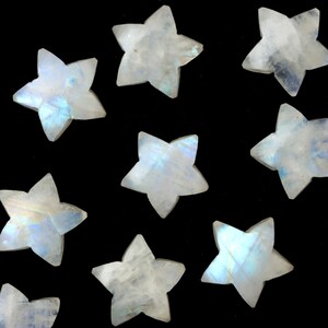 May include: A collection of star-shaped moonstone gemstones. The stones are white with iridescent blue and purple flashes, set against a black background. These polished stones are ideal for jewelry making or craft projects.