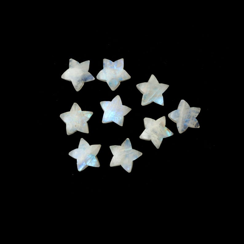 May include: Nine star-shaped moonstone gemstones with a pearly white and iridescent blue hue. The gemstones are scattered on a black background. These small, polished stones are ideal for jewelry making or craft projects.