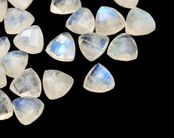 May include: A collection of triangular, faceted moonstone gemstones. The stones are mostly white with iridescent blue flashes, set against a black background. The gemstones are cut into a triangular shape.