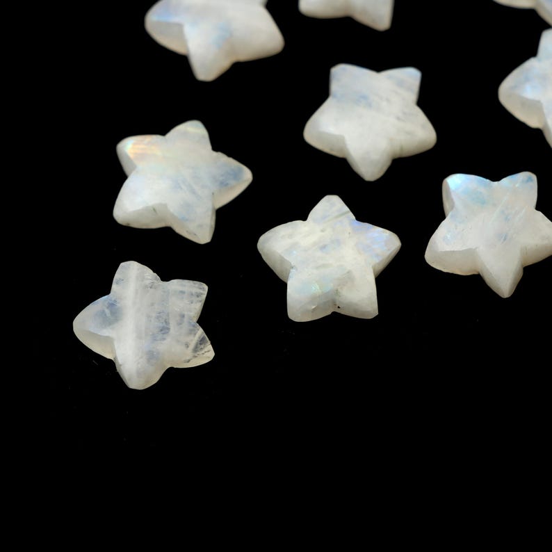 May include: A collection of small, star-shaped gemstones. The stones are a milky white color with iridescent flashes of blue and purple. The stars are scattered against a black background, creating a celestial effect. These gemstones are ideal for jewelry making or craft projects.