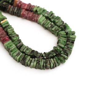 May include: Close-up of a strand of square-cut beads. The beads are a mix of green and red hues, with dark inclusions. The beads are strung together, creating a necklace or bracelet. The background is white.