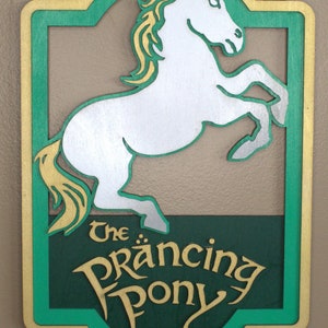 May include: A wooden sign with a green and gold background. The sign features a white silhouette of a horse rearing up on its hind legs. The text "The Prancing Pony" is written in gold lettering.