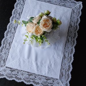 May include: A white lace tablecloth with a bouquet of cream-coloured roses in the centre.
