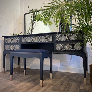 May include: A black vanity set with a gold patterned design. The set includes a mirror, a vanity table with drawers, and a stool. The vanity table has a dark blue velvet cushion on the top.