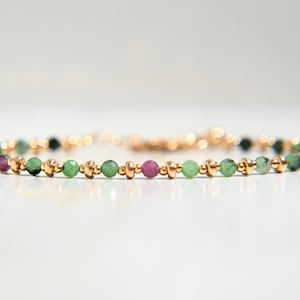 Op de afbeelding: Een delicate armband met kleine groene en roze edelsteen kralen afgewisseld met gouden kralen.