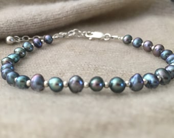 Op de afbeelding: Een zilveren kettingarmband met een rij donkerblauwe parels met een iriserende glans.