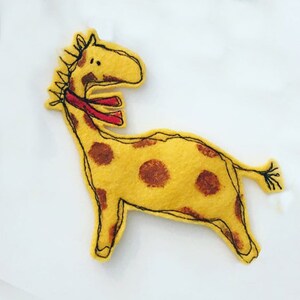 May include: A yellow felt giraffe with brown spots and a red scarf. The giraffe is embroidered with black thread.