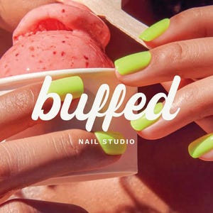 May include: Bright neon yellow manicured fingernails holding a white paper cup filled with a scoop of pink strawberry ice cream. The text buffed NAIL STUDIO is printed in white across the center of the image over the cup and fingers.