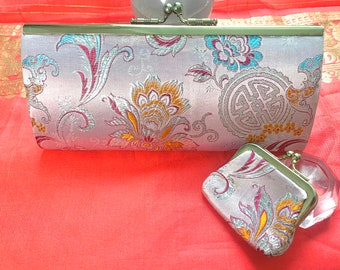 Puede incluir: Un conjunto de dos carteras de brocado plateado y dorado con motivos florales y geométricos. La cartera más grande tiene un cierre de broche y la cartera más pequeña tiene un cierre de presión.