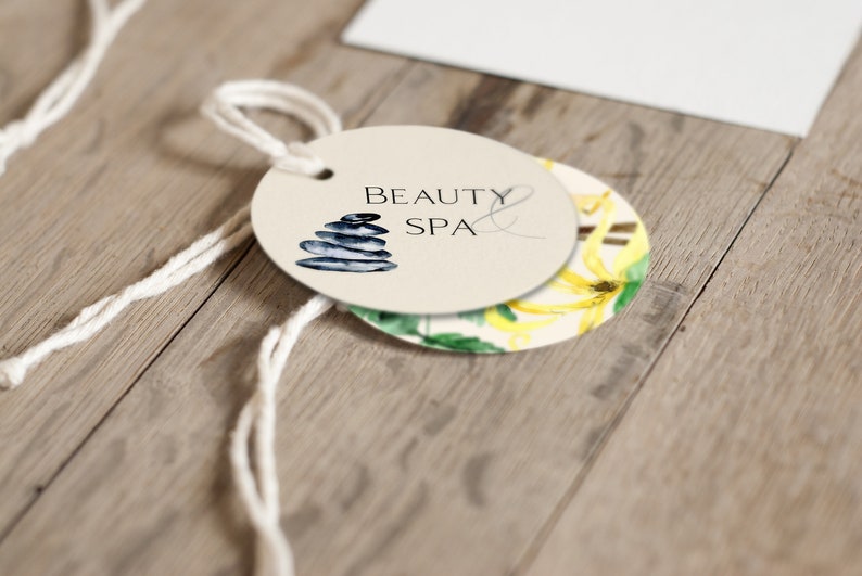 May include: A round, cream-colored tag with the text "Beauty & Spa" and a stack of gray stones. The tag is attached to a white string.