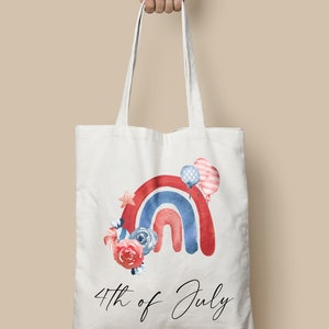 May include: A white tote bag with a red, white, and blue watercolor rainbow design. The rainbow is decorated with stars, flowers, and balloons. The text "4th of July" is printed below the rainbow.