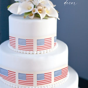 May include: A white wedding cake decorated with American flags. The cake is topped with white calla lilies.