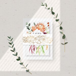 May include: A set of white cards with a watercolor floral design featuring proteas, eucalyptus, and other flowers. The cards are tied together with a gold ribbon with a floral design and the word "AJIRA" printed on the ribbon.