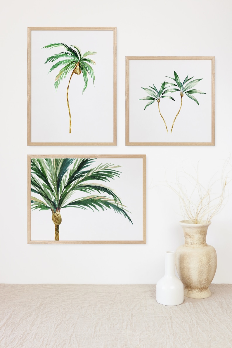 May include: Three framed watercolor paintings of palm trees on a white wall. The paintings are in wooden frames with a natural wood finish. The paintings are arranged in a vertical row, with the largest painting at the top and the smallest painting at the bottom.