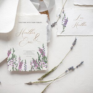 May include: Elegant wedding stationery set featuring a main invitation with the names "Heather & Eric" in gold script, surrounded by watercolor lavender. Includes matching cards and envelopes, with dried lavender sprigs.
