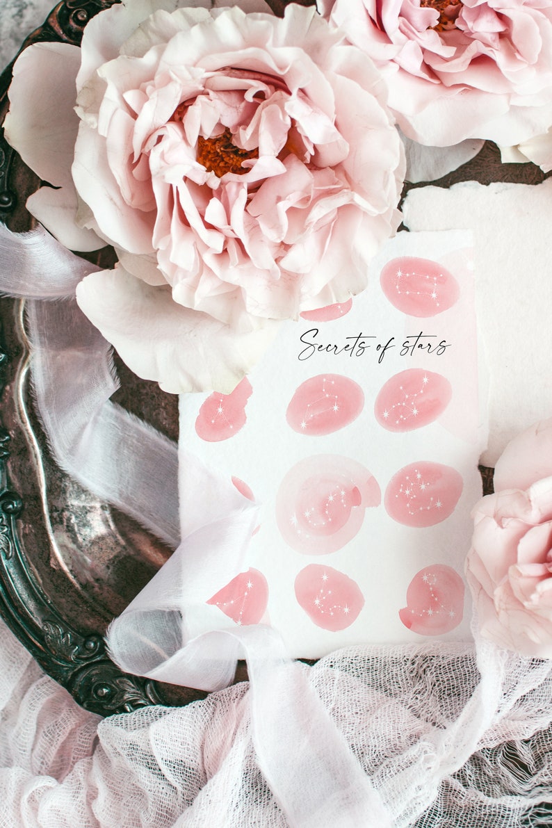 May include: A white card with pink watercolor circles featuring constellations and the text "Secrets of stars". The card is surrounded by pink flowers and white fabric.