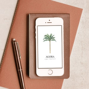 May include: A white smartphone with a brown leather case. The phone screen displays a logo for Agora spa hotel, featuring a green palm tree on a white background.