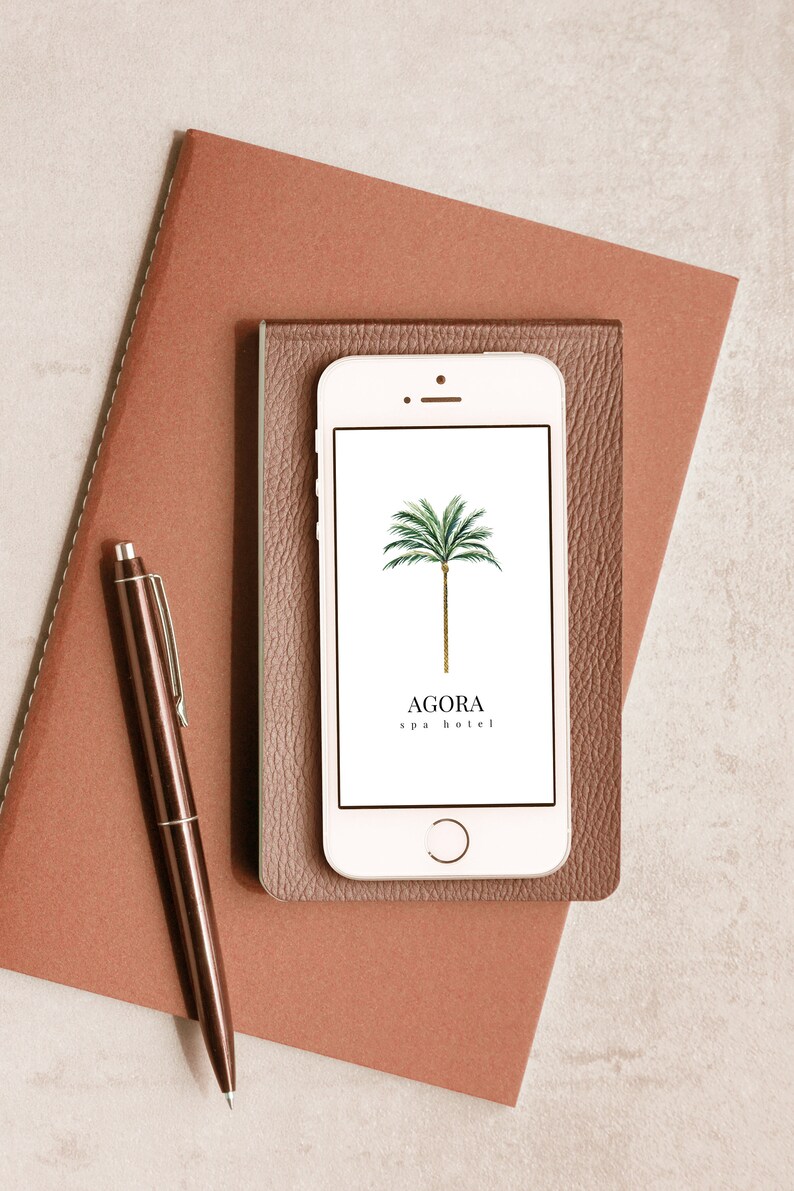 May include: A white smartphone with a brown leather case. The phone screen displays a logo for Agora spa hotel, featuring a green palm tree on a white background.