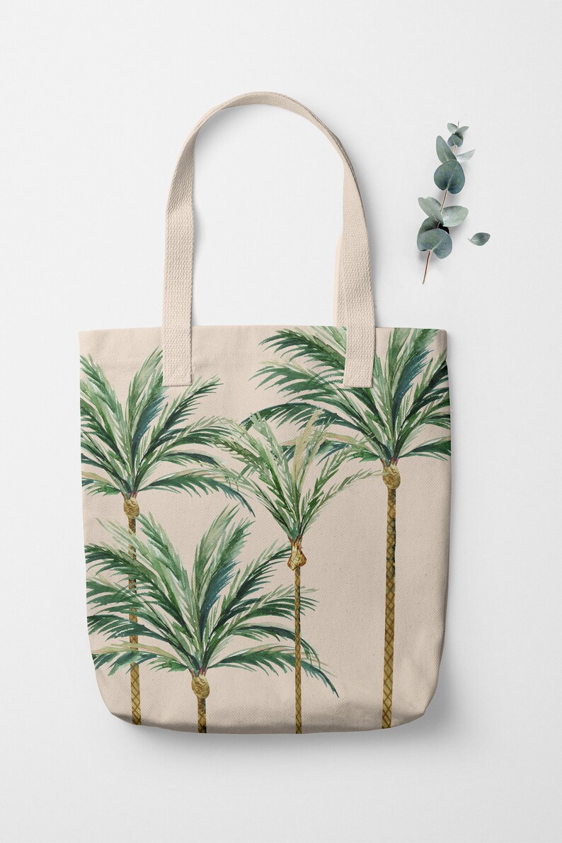 May include: A beige canvas tote bag with a design of four green palm trees on a beige background.