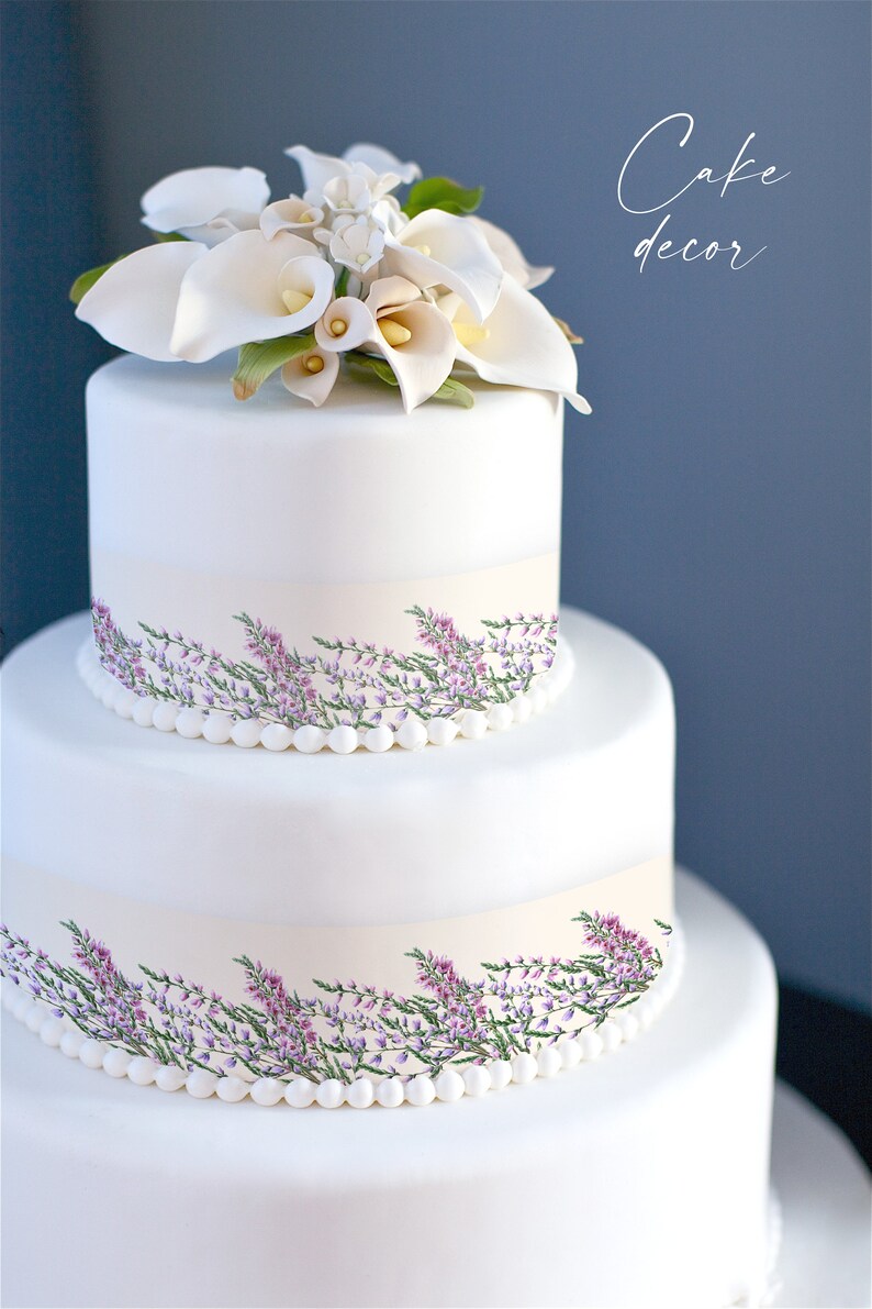 May include: A three-tiered white cake decorated with a floral arrangement of white calla lilies and other flowers. The cake has a band of light beige with a floral design of purple flowers and green leaves. The text "Cake decor" is written on the right side.