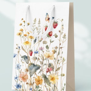 Op de afbeelding: Witte cadeauzak met een aquarelontwerp van wilde bloemen, vlinders en aardbeien. De tas heeft witte touwhandvatten.