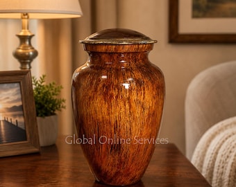 Op de afbeelding: Een decoratieve urn met een rijke, warme bruine afwerking en een verticaal houtnerfpatroon. De vaas heeft een afgerond lichaam dat naar de basis toe taps toeloopt en is bekroond met een gladde, donkerbruine deksel met een goudkleurige rand.