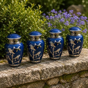 May include: Four small, deep blue metal urns with silver-toned lids and bases. Each urn features a detailed silver inlay design depicting birds perched on branches. The urns are arranged in a row, showcasing a polished finish and metallic accents.