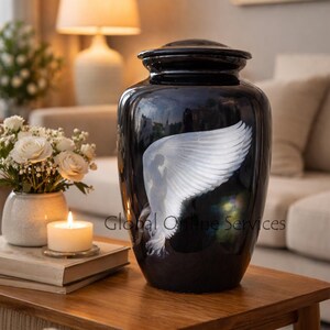 Peut inclure: Urne noire brillante avec un motif d'aile d'ange blanche. L'urne cylindrique est dotée d'un couvercle et est présentée sur une table en bois. Le texte "Global Online Services" est visible sur l'urne.