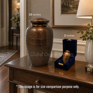 May include: A large, dark bronze-colored metal cremation urn with an intricate floral engraving, labeled 10 inches, alongside a smaller matching keepsake urn in a blue velvet-lined box, labeled 3 inches, with text stating it is for size comparison.