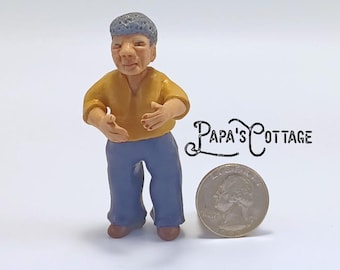 May include: A miniature figurine of a person wearing a yellow shirt and blue pants. The figurine has a blue cap and is standing next to a quarter coin. The text "Papa's Cottage" is visible.