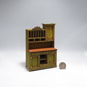 May include: A miniature green painted wooden hutch with a top shelf, open shelves, and a lower cabinet with two doors and drawers. The hutch is about the size of a US quarter.