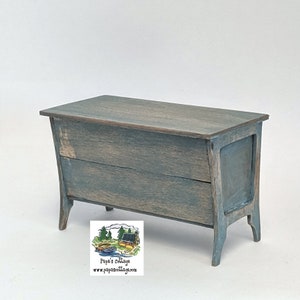 May include: A blue wooden chest with a distressed finish and two drawers. The chest has a simple design with rounded edges and sits on four legs.