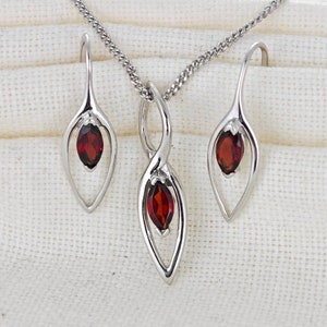 May include: A silver necklace and earrings set with a red gemstone pendant and matching earrings. The pendant is a twisted design with a marquise-shaped gemstone. The earrings are simple drop earrings with a marquise-shaped gemstone.