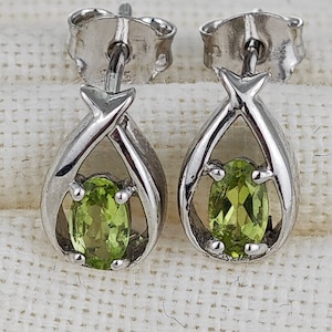May include: A pair of silver earrings with a green oval gemstone in each. The earrings have a simple, elegant design.