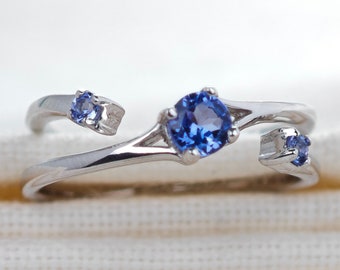 May include: A silver ring with three blue sapphires. The ring is open and has a delicate design.