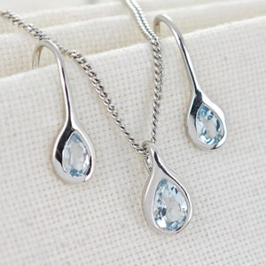 May include: A silver necklace and earrings set with teardrop-shaped pendants featuring light blue gemstones.