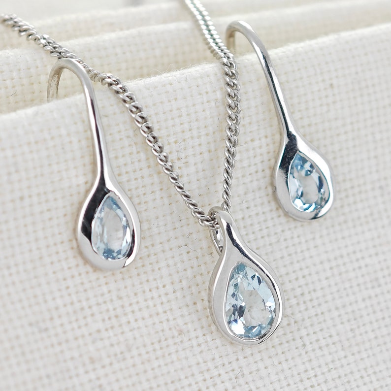 May include: A silver necklace and earrings set with teardrop-shaped pendants featuring light blue gemstones.