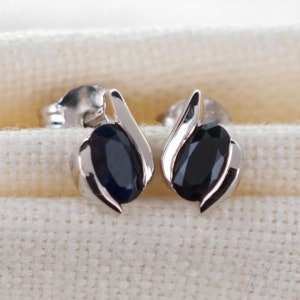May include: A pair of silver stud earrings with black oval-shaped gemstones.