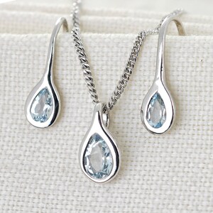 May include: A silver necklace and earrings set with teardrop-shaped blue gemstones.
