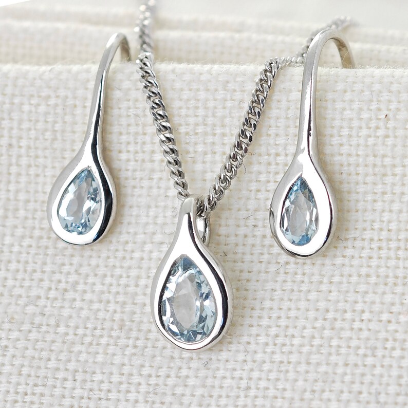 May include: A silver necklace and earrings set with teardrop-shaped blue gemstones.
