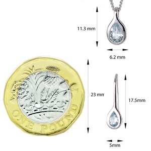 May include: A silver pendant featuring a light blue teardrop-shaped aquamarine gemstone. The pendant measures 11.3 mm in height and 6.2 mm in width. The pendant is displayed alongside a British one pound coin to illustrate its size.