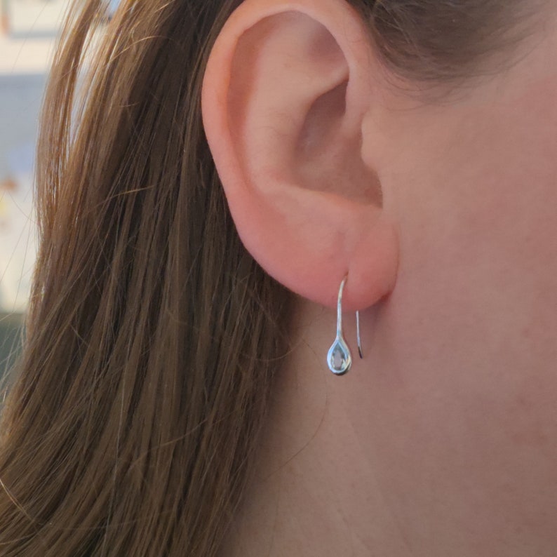 May include: A pair of silver teardrop earrings with a small clear stone in the centre of each teardrop.