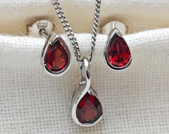 May include: A silver necklace and earrings set with teardrop-shaped red gemstones. The necklace features a delicate chain and a pendant with a twisted design.