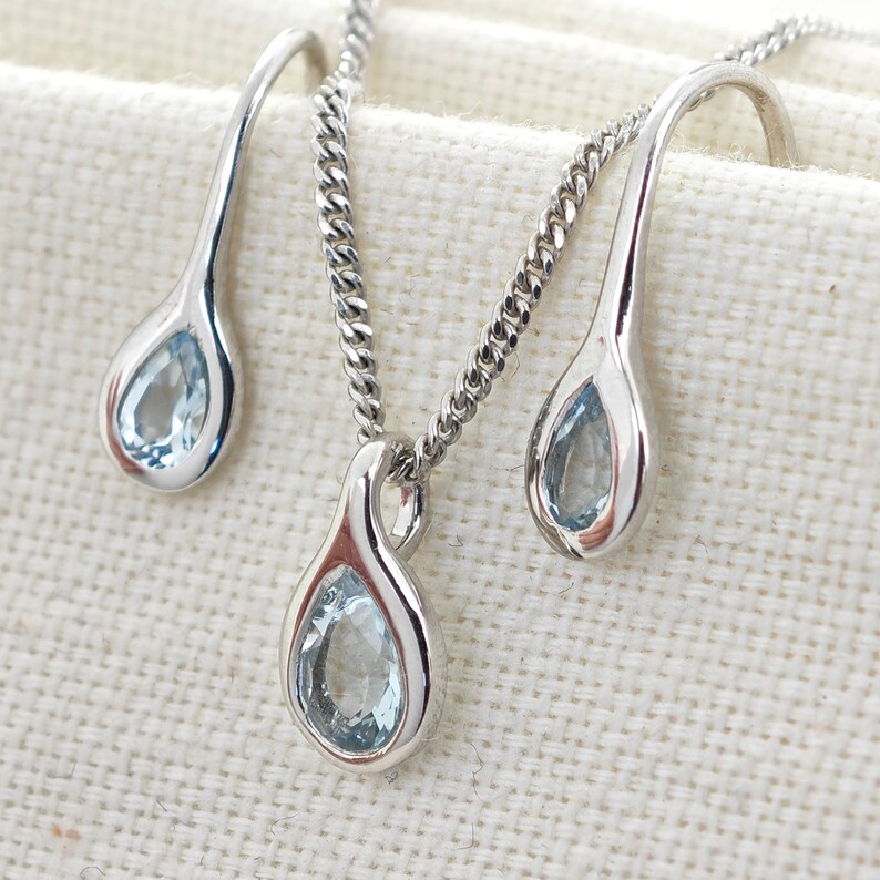 May include: A silver necklace and earrings set with teardrop-shaped blue gemstones.