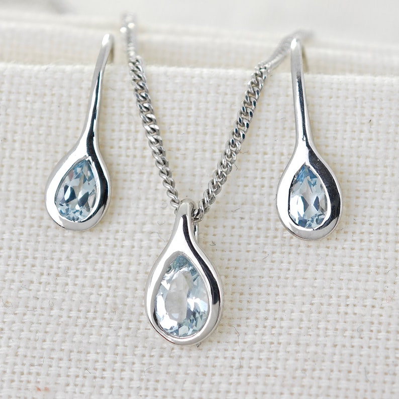 May include: A silver necklace and earrings set with teardrop-shaped aquamarine stones.