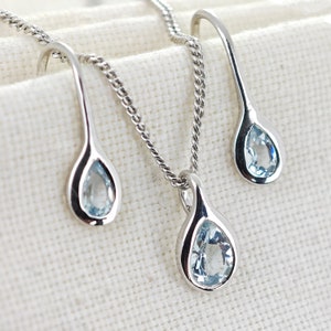 May include: A silver necklace and earrings set with teardrop-shaped pendants featuring light blue aquamarine gemstones.