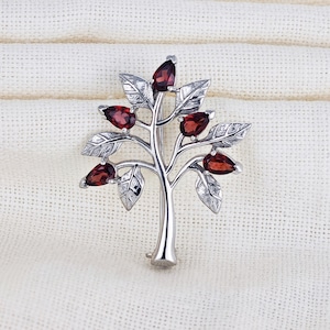 May include: A silver tree brooch with red gemstone leaves. The brooch is a delicate and intricate design.