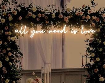May include: A wedding reception venue decorated with floral arrangements and a neon sign that reads "all you need is love".