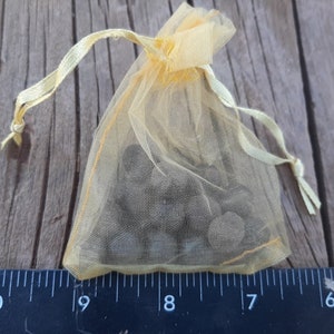 May include: A small yellow drawstring bag filled with small, dark gray stones. The bag is made of a sheer fabric and is sitting on a wooden surface.