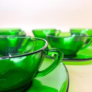 Peut inclure: Un ensemble de tasses et soucoupes en verre vert émeraude. Les tasses ont des anses incurvées et reposent sur des soucoupes rondes assorties. La finition brillante reflète la lumière. Un service à thé classique.